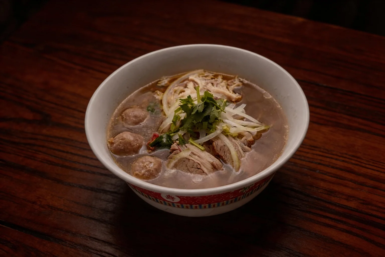 Special phở soup in a white bowl with a red border, on a dark wooden table