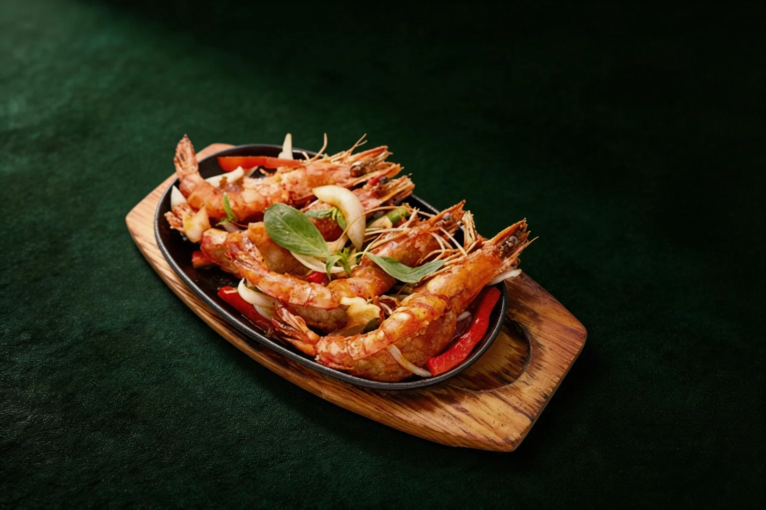 King prawns with basil leaves on a cast-iron plate and wooden board, dark green background