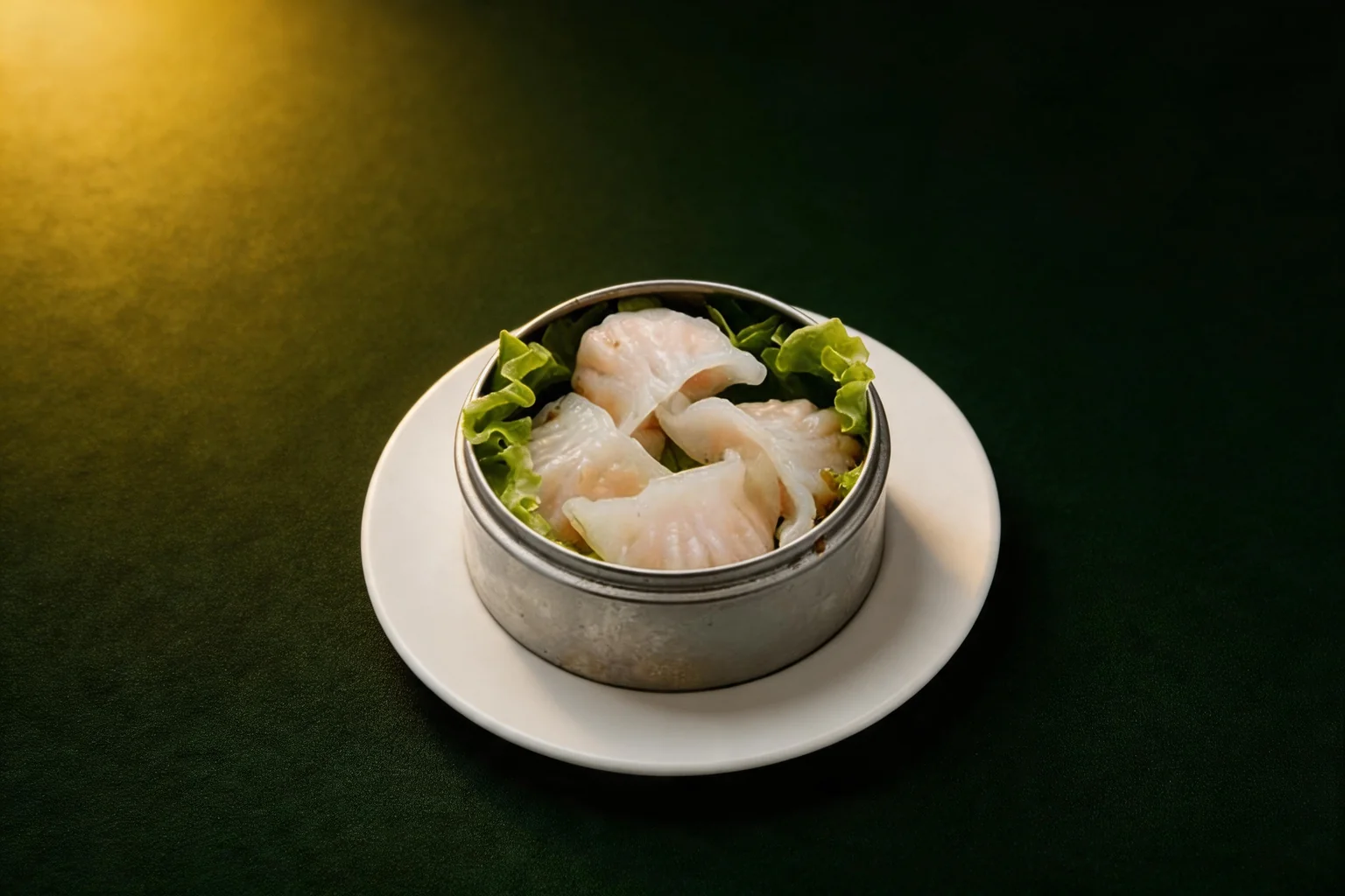 Shrimp dumplings in a metal steamer basket on a white plate, dark green background